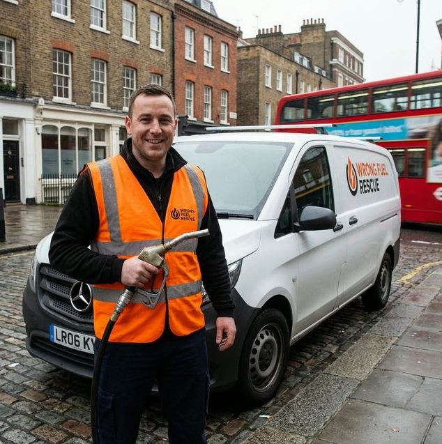 Wrong Fuel Rescue technician holding a fuel nozzle beside the mobile fuel drain van on a London street